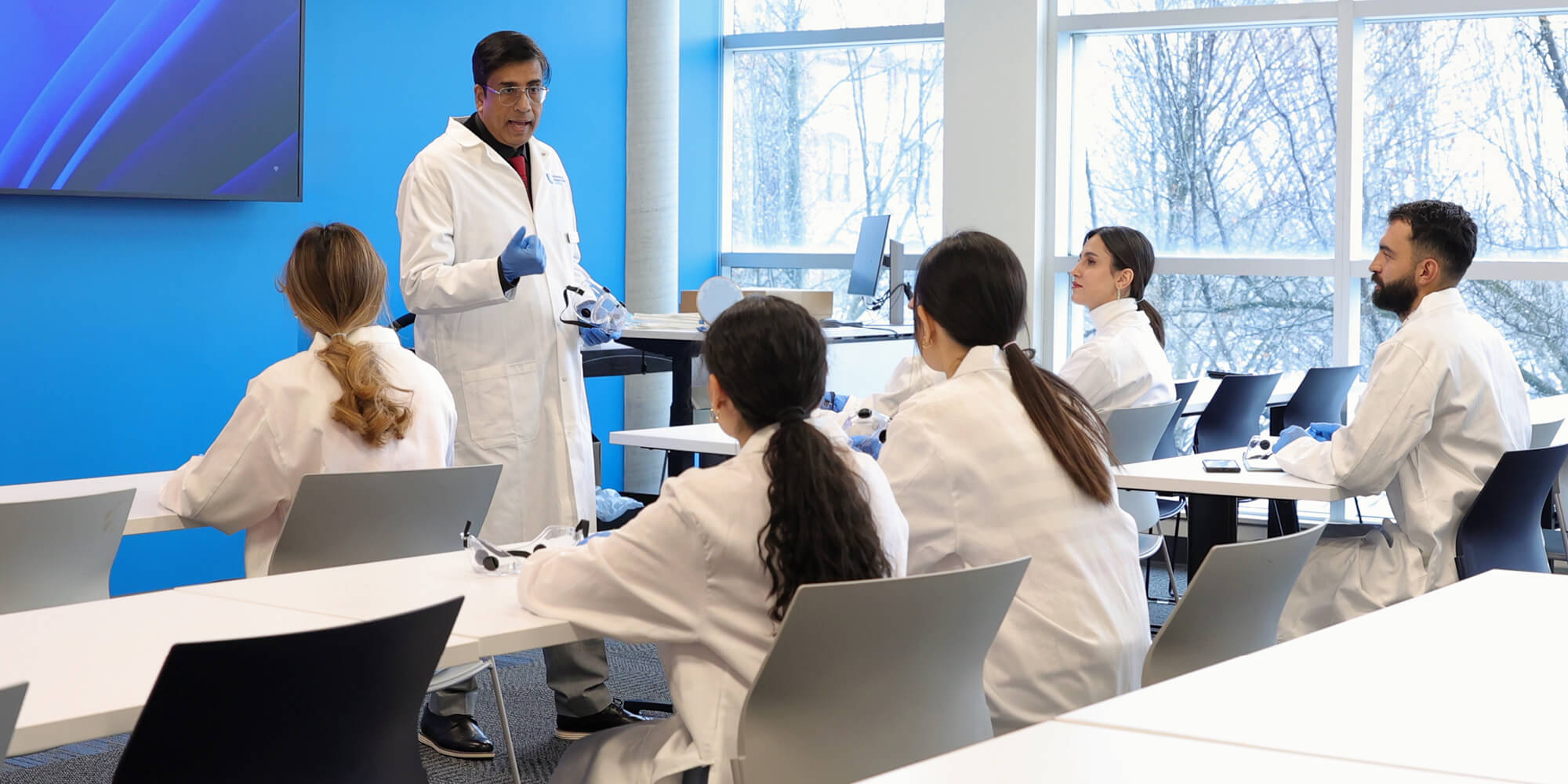 A group of individuals in lab coats engaged in discussion while seated at tables in a laboratory setting