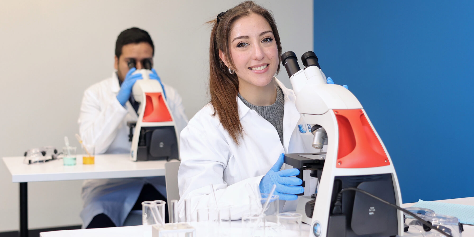 A female student in a lab coat in front of a microscope on a laboratory setting
