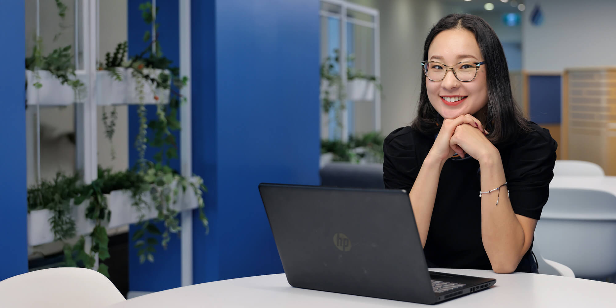 A female student with a laptop sitting at the cafeteria looking at the camera