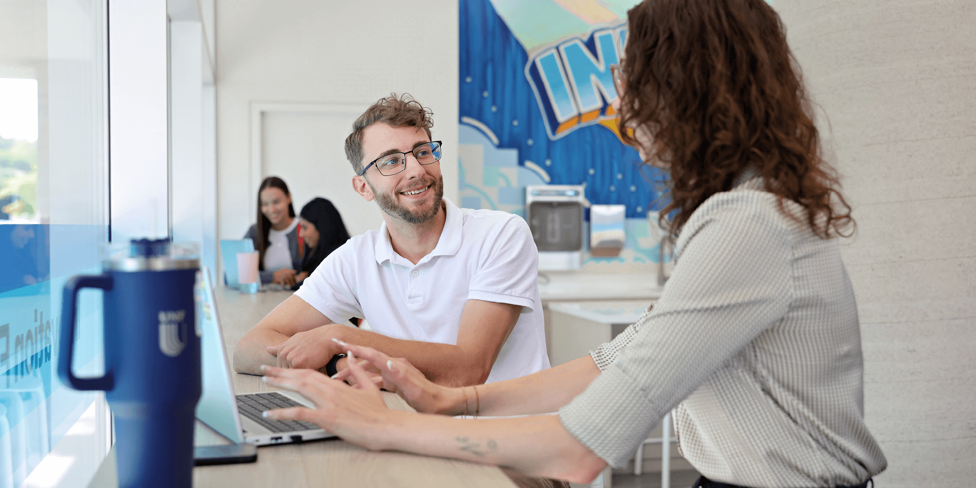 Two students talking in front of a laptop
