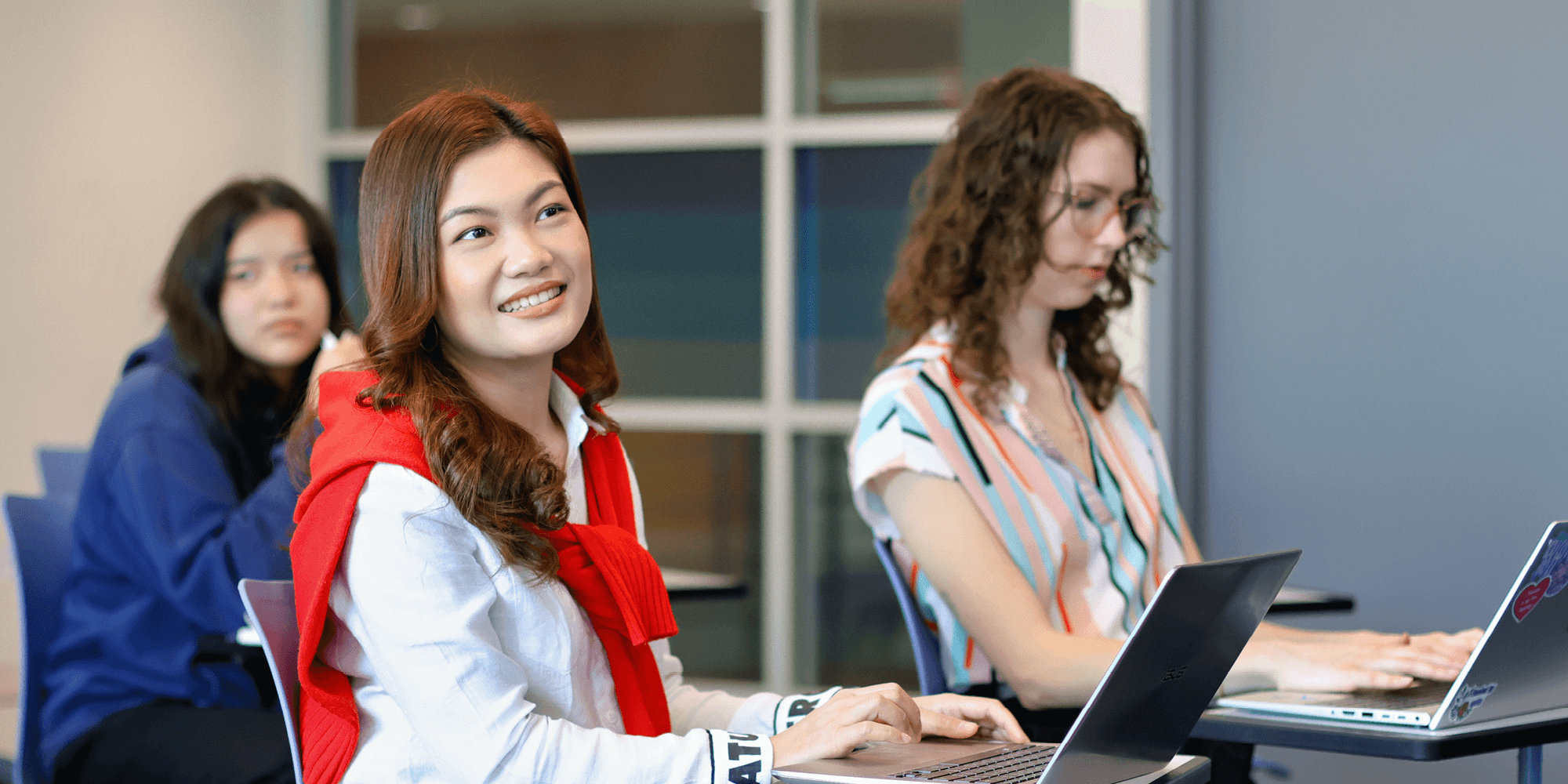 Three female students with laptops in a classroom setting inside UNFC campus